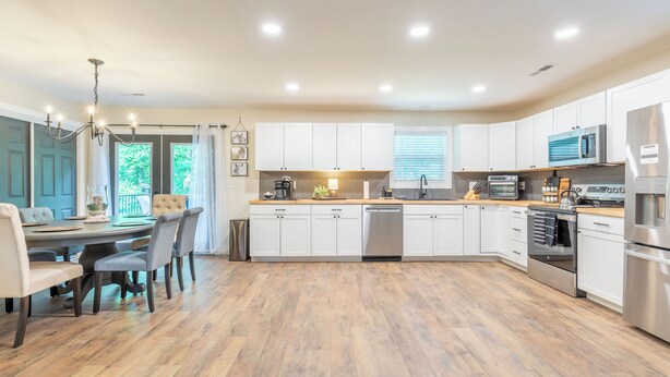 Una cocina moderna con armarios blancos, electrodomésticos de acero inoxidable y un comedor con candelabro.