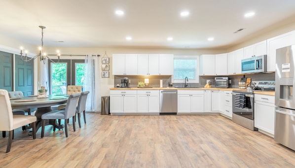 A modern kitchen with white cabinets, stainless steel appliances, and a dining area with a chandelier.