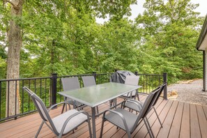 A deck with a table and chairs, surrounded by a railing, overlooking a forested area.