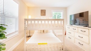 Una cama litera con escritorio, cómoda, televisor y ventana con persianas.