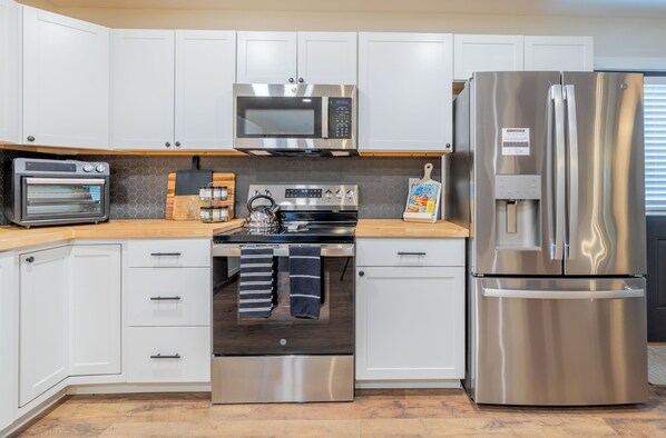 Una cocina moderna con armarios blancos, un refrigerador de acero inoxidable, un microondas, una estufa y un horno.