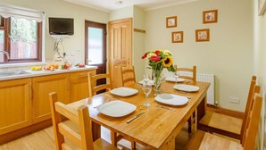 Comedor con una mesa de madera dispuesta para cuatro personas, rodeada de sillas, y un jarrón de flores sobre la mesa.