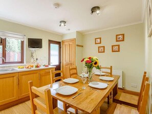 A dining area with a wooden table set for four, surrounded by chairs, with a vase of flowers on the table. - 4 Bed in Harlech (oc-89631) (Harlech)