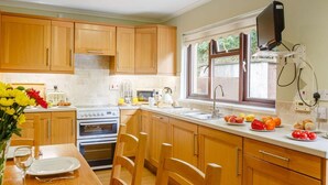 Una cocina con armarios de madera, estufa, pileta y ventana con vista a la vegetación.