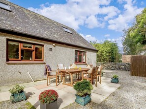 A stone house with a tiled patio, a wooden table, and chairs.