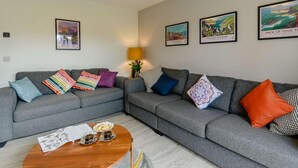 A modern living room with a grey sofa, colorful cushions, a wooden coffee table, and framed artwork on the walls. - 3 Bed in Narberth (oc-89627) (Templeton)