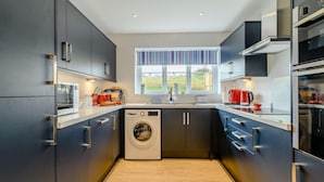 A compact kitchen with a built-in washer, a window with striped curtains, and modern cabinetry. - 3 Bed in Narberth (oc-89627) (Templeton)