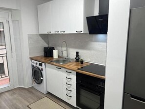 A compact kitchen with a washing machine, a sink, and a stove. - Apartment in Amer (Amer)
