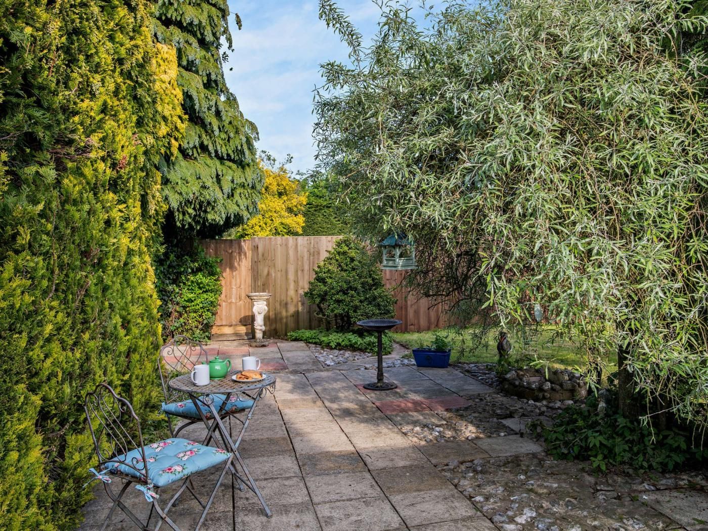 A patio area with a table and chairs, surrounded by lush greenery and a wooden fence.