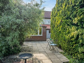 A patio with a table and chairs, a bird bath, and a hedge. - 3 Bed in Melton Constable (oc-90184) (Briston)