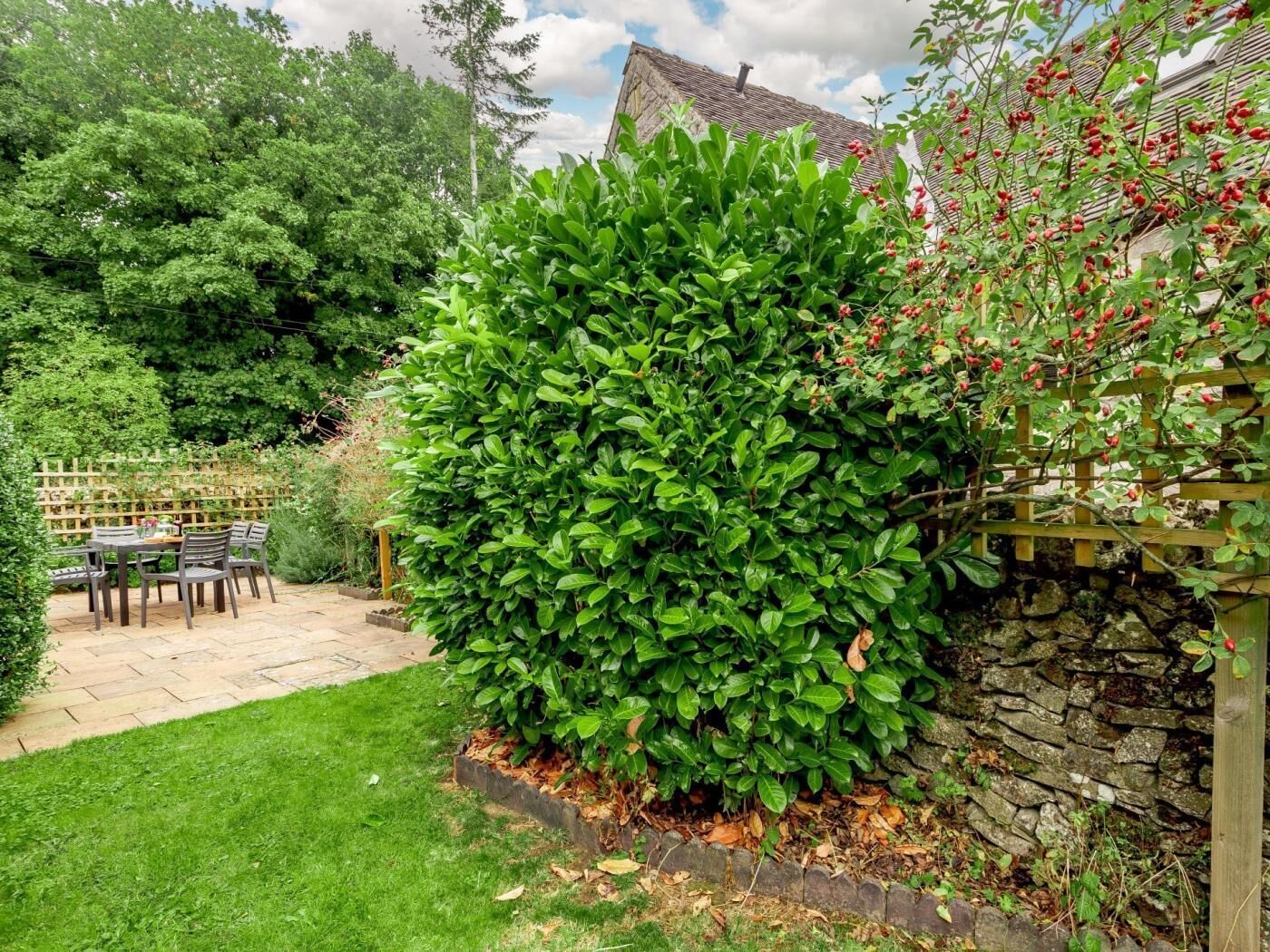Ein gepflegter Garten mit Steinmauer, Holzzaun und einer Terrasse mit Gartenmöbeln.