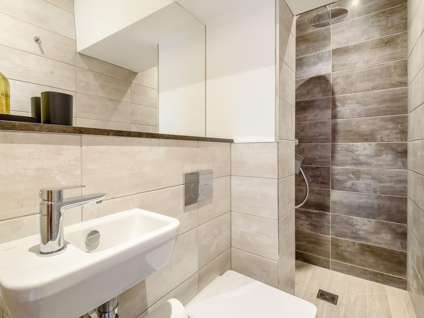 A modern bathroom with a white sink, a mirror, and a shower area.