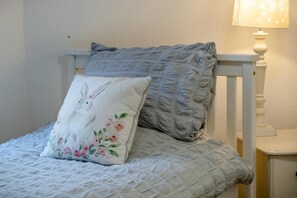 A bed with a white quilt and two pillows, one with a floral design and the other with a textured pattern.
