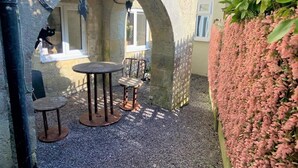 Un espacio al aire libre con mesas y sillas, un arco y una pared cubierta de flores rosadas.