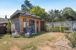 A small wooden cabin with a patio area, two folding chairs, and a table.