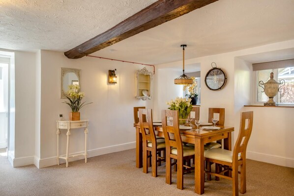 A dining area with a wooden table and chairs, a wall-mounted clock, and a window with a view. - 3 Bed in Ventnor (oc-89972) (Niton)