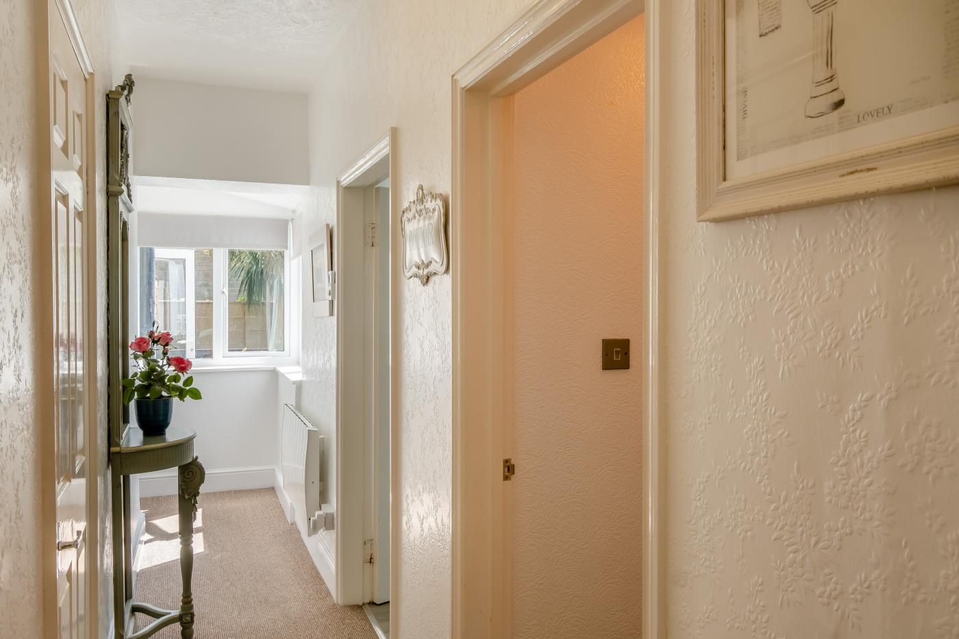 A hallway with a radiator, a door with a light switch, and a window with a view of greenery.