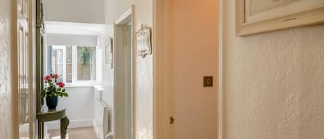 A hallway with a radiator, a door with a light switch, and a window with a view of greenery.