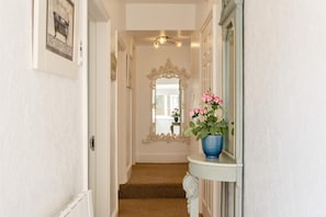 A hallway with a mirror, a blue vase with flowers, and a patterned carpet. - 3 Bed in Ventnor (oc-89972) (Niton)