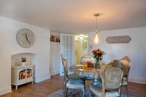 Un coin repas avec une table ronde, des chaises, une horloge, une cheminée et un panneau décoratif au mur.