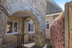 Un bâtiment en pierre doté d’une arche, d’une table et d’un mur recouvert de fleurs roses.