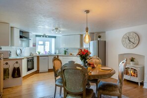 A modern kitchen with a dining area, featuring a round table, chairs, a hanging light fixture, and a clock on the wall.