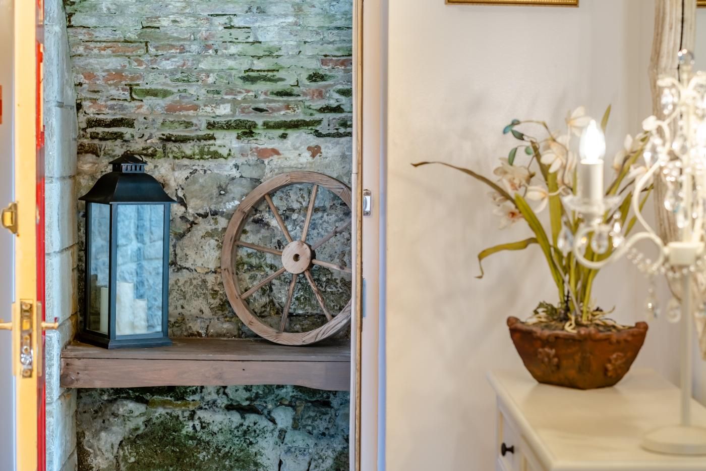 A rustic interior with a stone wall, a lantern, a wooden wheel, and a potted plant.
