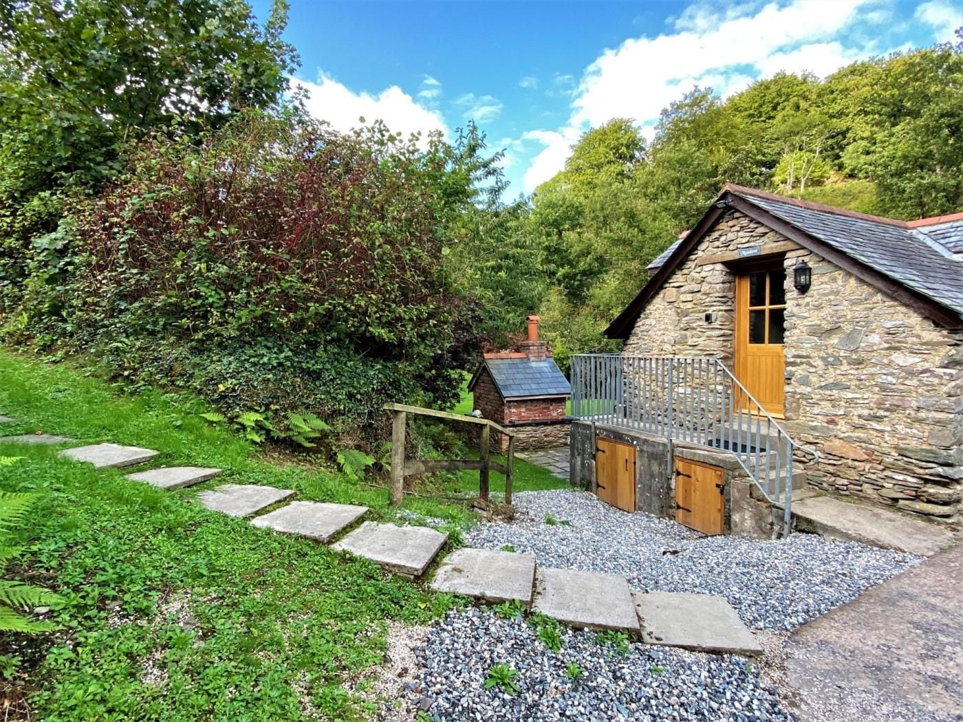 A stone cottage with a wooden door, a gravel pathway leading to it, and a metal fence.