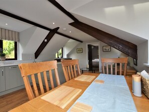 A dining area with a long wooden table, chairs, and a view of a kitchen and bedroom through an open doorway. - 1 Bed in Barnstaple (oc-89767) (Parracombe)