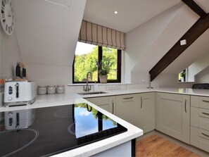 A modern kitchen with a built-in stove, a window with a view of greenery, and a white countertop. - 1 Bed in Barnstaple (oc-89767) (Parracombe)