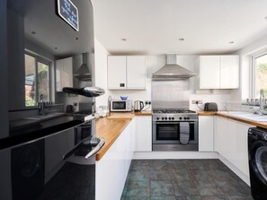 A modern kitchen with white cabinets, a stainless steel range hood, a built-in oven, a microwave, and a washing machine. - 5 Bed in Ilfracombe (oc-89563) (Ilfracombe)