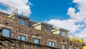 Un edificio de varios pisos con paredes de piedra, balcones con barandillas de metal y ventanas.