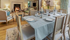 Een eetgedeelte met een open haard, een tafel gedekt voor vier personen, en een gezellige woonkamer op de achtergrond.