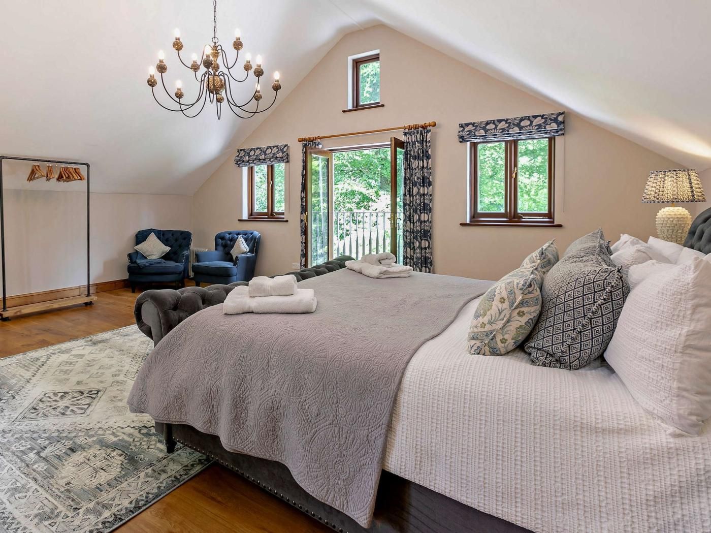 Une chambre avec un grand lit, deux fauteuils, un lustre et une vue sur la verdure.