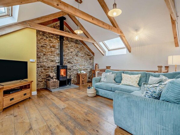 Ein gemütliches Wohnzimmer mit Steinwand, Holzbalken, einer Couch, einem Fernseher und einem Kamin.