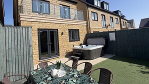 Una casa de dos pisos con un patio que tiene una mesa, sillas y un jacuzzi.