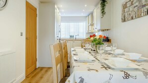 Comedor con una mesa larga dispuesta para seis, sillas de madera y un florero con flores.