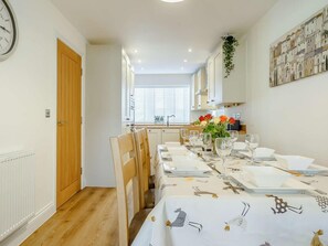 A dining area with a long table set for six, wooden chairs, and a vase with flowers. - 4 Bed in Whitby (oc-89533) (Whitby)
