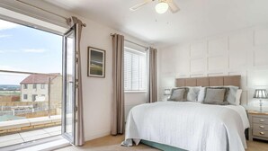 Un dormitorio con una cama grande, un ventilador de techo, una ventana con cortinas y vistas a edificios.