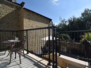 En bygning i sten med balkon, metalgelænder og et bord med stole.