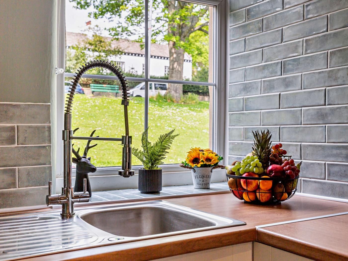 Eine Küche mit Spüle aus Edelstahl, einem Fenster mit Gartenblick und einer Obstschale auf der Arbeitsfläche.