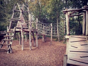 Eine Holzspielanlage mit einer Seilbrücke und Kletterelementen in einem bewaldeten Gebiet.