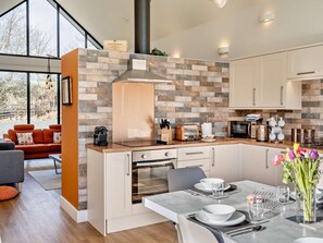 A modern kitchen with a brick backsplash, a built-in oven, and a dining area with a table set for two. - 3 Bed in Bamburgh (oc-90062) (Bamburgh)