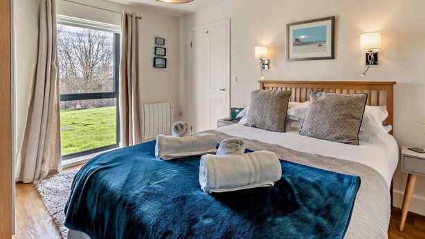 Ett hotellrum med en säng, två sänglampor, ett fönster med gardiner, utsikt över omgivningarna och en inramad tavla på väggen.