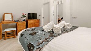 Een slaapkamer met een bed, een bureau met een televisie, een stoel en een spiegel.