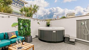 Een dakterras met een jacuzzi, een bank, een salontafel en een bioscoopbord in de verte.