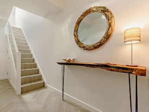 Eine Treppe mit einer weißen Wand und einem hölzernen Konsolentisch mit Spiegel und Lampe.