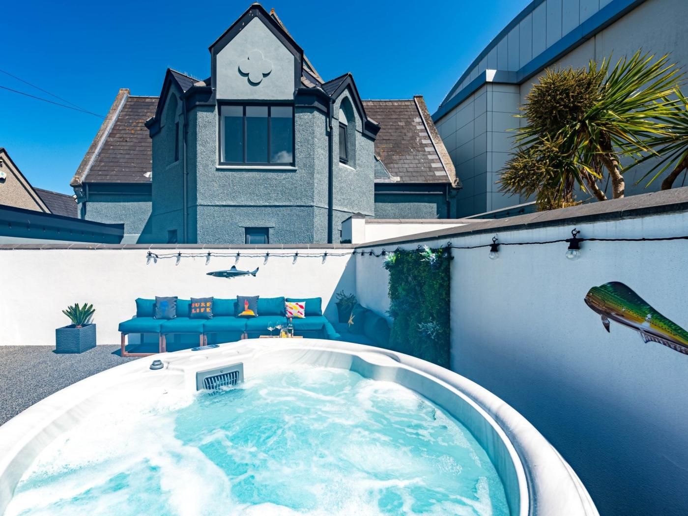 A hot tub in a backyard with a blue couch and a house in the background.