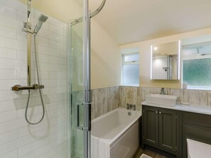 Un baño con ducha de vidrio, bañera blanca y tocador con espejo.