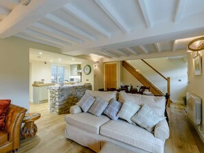 Un salon avec un canapé, une table basse en bois, un mur en pierre, une cuisine à l’arrière-plan et un escalier.